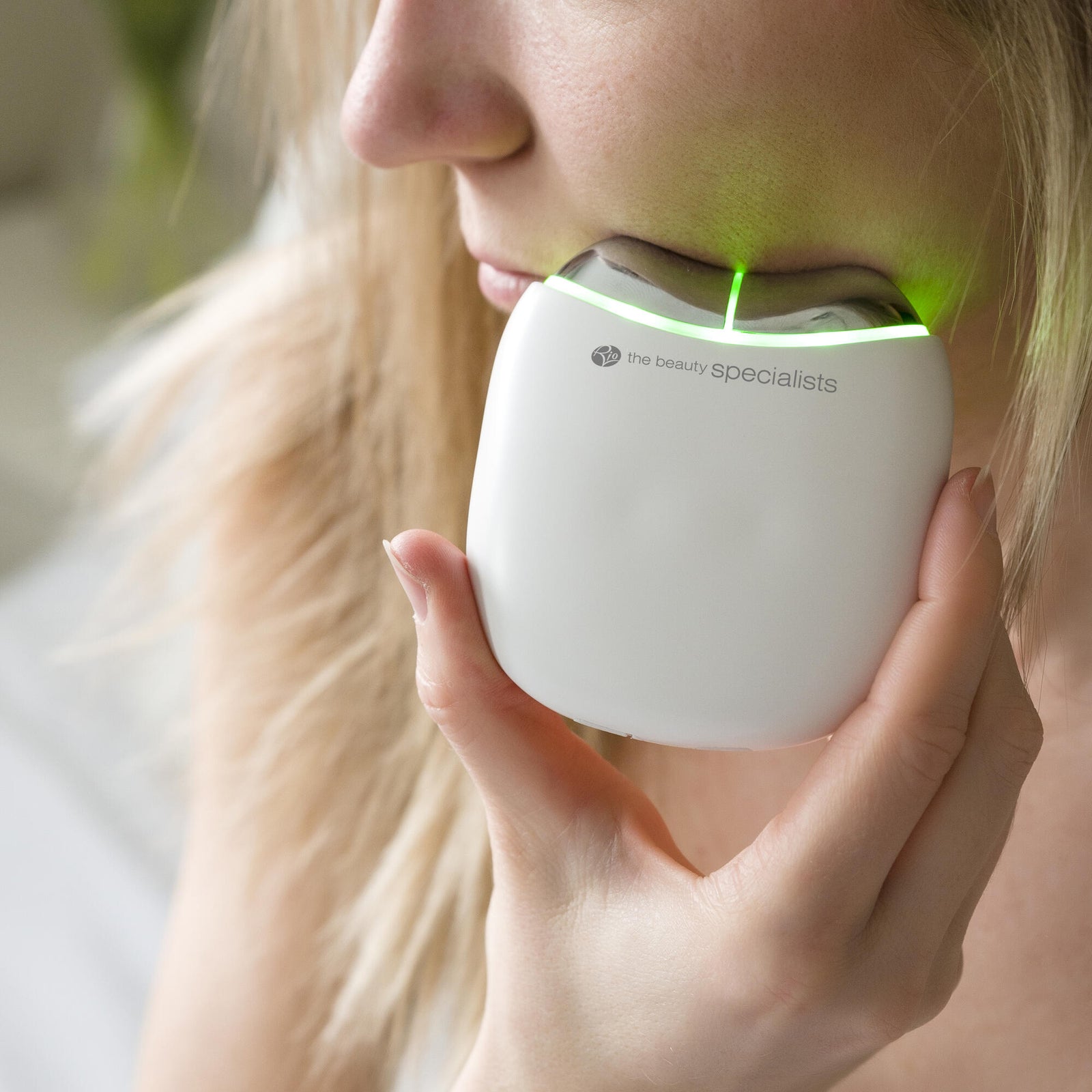 A woman holds the Rio Face Lift & Tone Facial Toner with green LED lights against her jawline, using it as an anti-aging skincare device for effective facial toning.