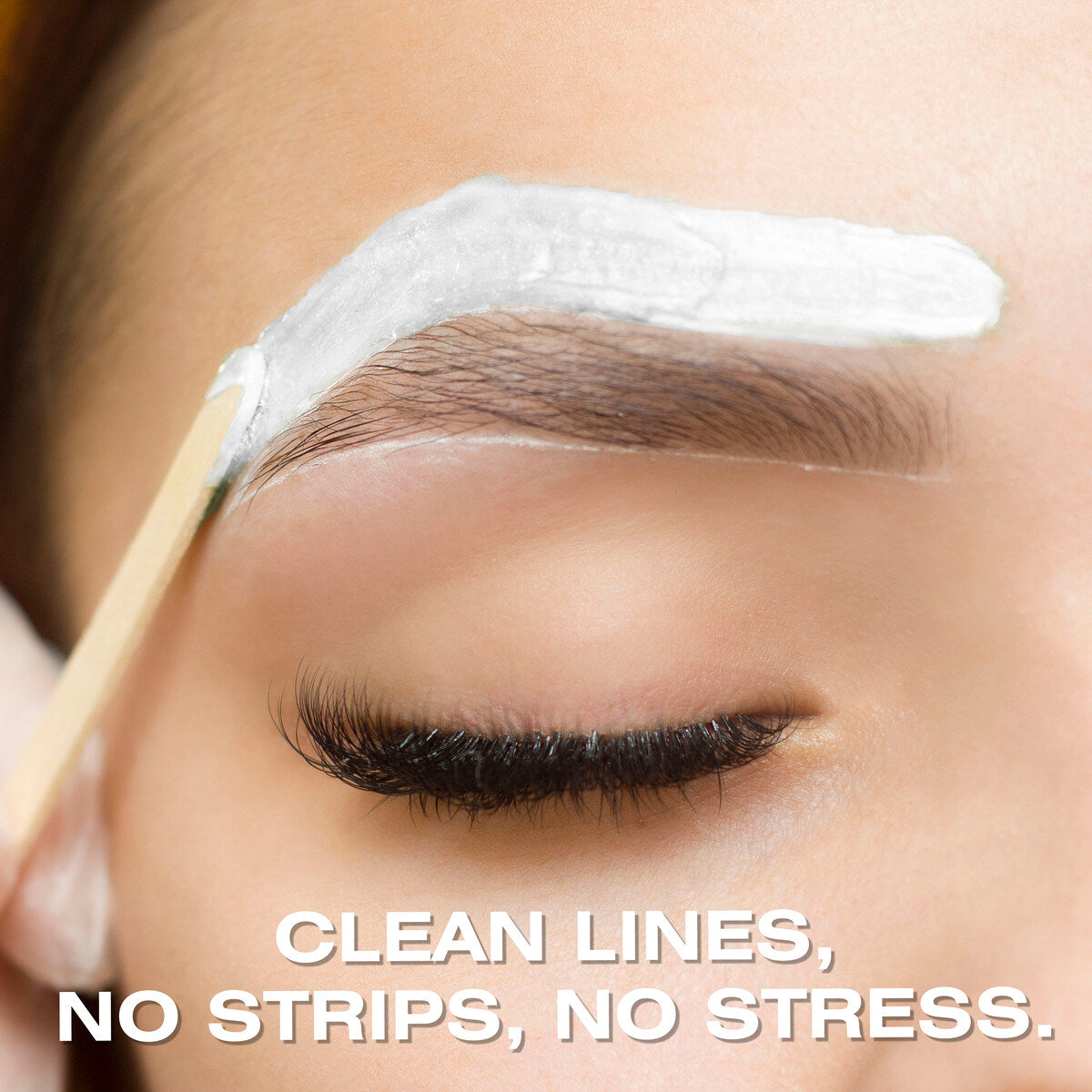 A close-up of a person’s closed eye as Rio Coconut Go Smooth Stripless Hard Wax Beads (100g) are applied above their eyebrow with a wooden stick. Text at the bottom reads, CLEAN LINES, NO STRIPS, NO STRESS.