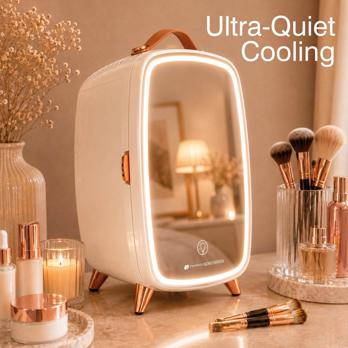 A compact Rio Beauty Skincare Fridge With Mirror, featuring a sleek white design, mirrored door, and LED lighting, sits on a vanity surrounded by makeup brushes, skincare products, and a glowing candle. Ideal for keeping cosmetics and creams fresh and cool, it ensures your beauty essentials are always ready to use. Text reads: Ultra-Quiet Cooling.