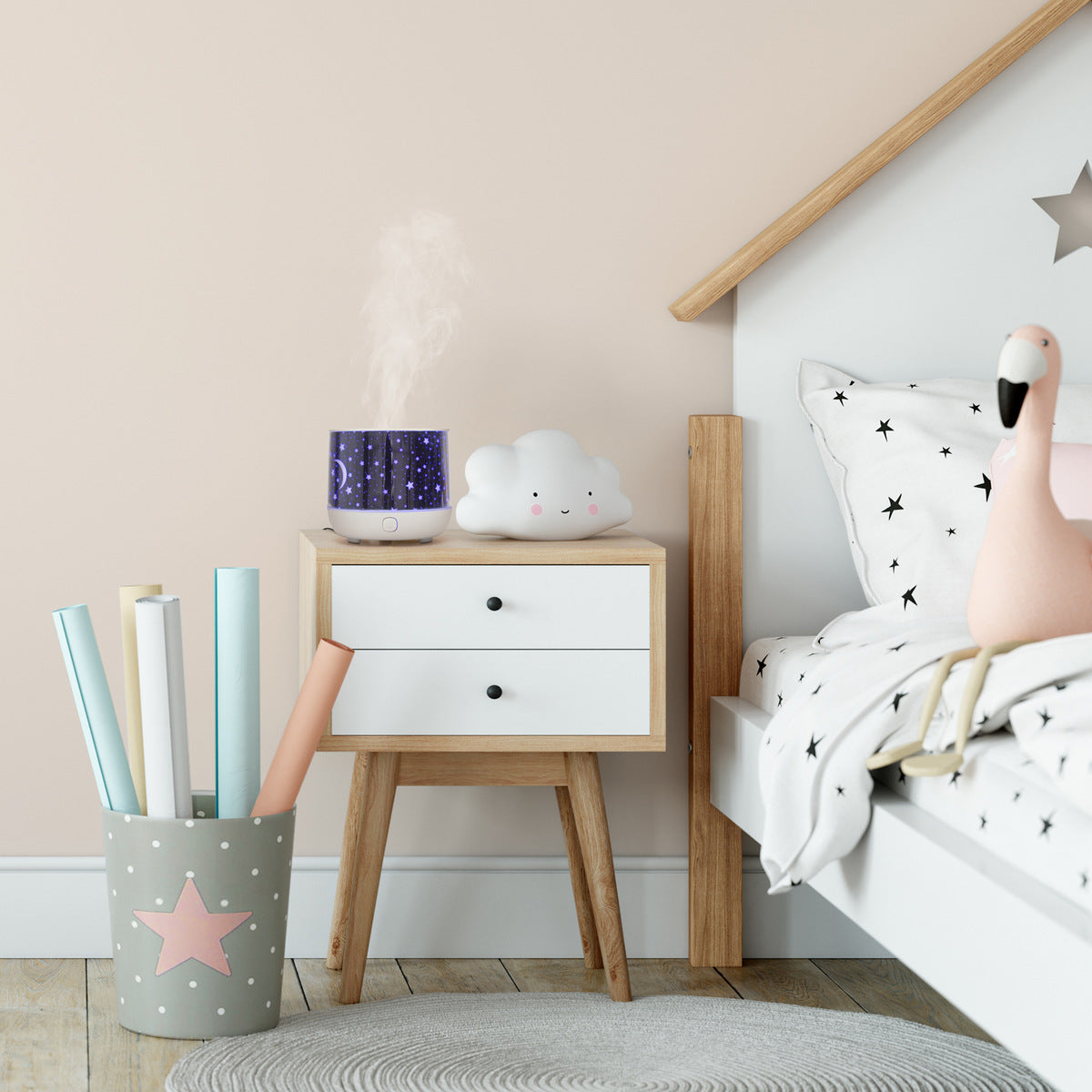 A children’s bedroom features a Rio Dream Time Aroma Diffuser, Humidifier and Night Light on the bedside table, alongside star bedding, a pink flamingo plush on the bed, and a bucket of rolled papers nearby.