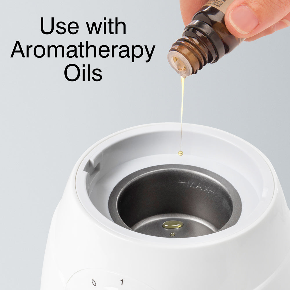 A hand pours aromatherapy oil from a small brown bottle into the metal reservoir of the Rio Facial Sauna Skincare with Steam Inhaler. Text above reads, Use with Aromatherapy Oils.