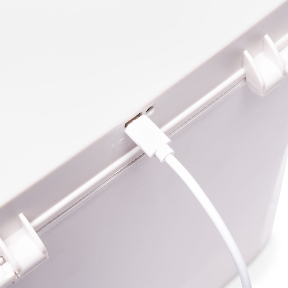 A close-up of a white USB cable plugged into the Ultimate Beauty Storage Box With Dimmable Mirror by Rio, a white plastic makeup organizer featuring latches on the lid.