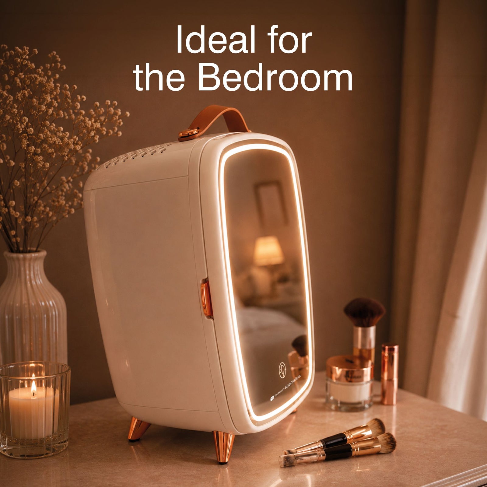 A Rio Beauty Skincare Fridge With Mirror featuring a mirrored door and LED lights sits on a bedroom vanity beside cosmetics, makeup brushes, a candle, and a vase; text reads: Ideal for the Bedroom and perfect for chilled storage of your favorite creams.