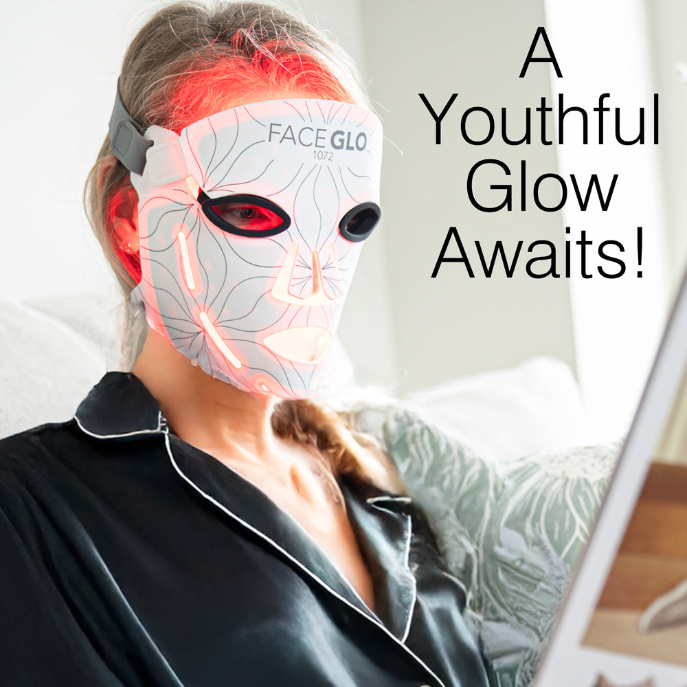 A person in dark pajamas with white trim reclines on a couch, reading a tablet while wearing the Rio FaceGLO mask. Text reads: A Youthful Glow Awaits! The mask emits clinically effective light for radiant skin.