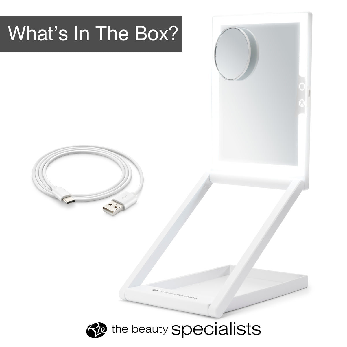 The Rio Home & Away Dressing Table Make Up Mirror is a foldable white mirror with a height-adjustable circular magnifier and detachable USB cable. Whats In The Box? appears in text, with the beauty specialists logo at the bottom.