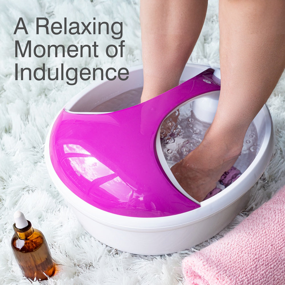 A person enjoys a soothing soak with the Rio Deluxe Foot Spa Bath and Massager - Purple on a fluffy rug, accompanied by a pink towel and oil. Text reads: A Relaxing Moment of Indulgence.