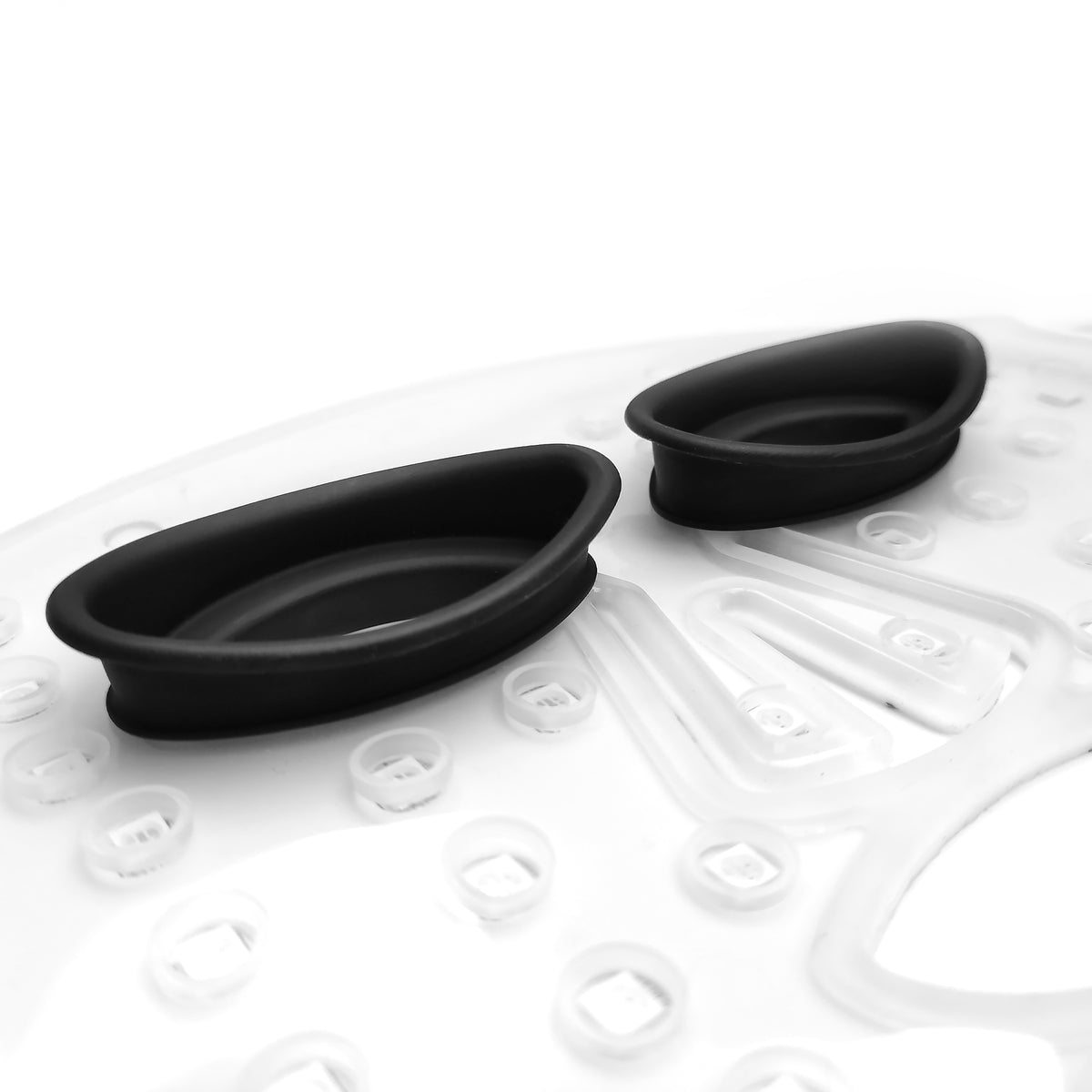 Close-up of two black oval-shaped silicone FaceLite Eye Shields by Rio on a white textured plastic surface with raised bumps—likely part of FaceLite or its accessories.