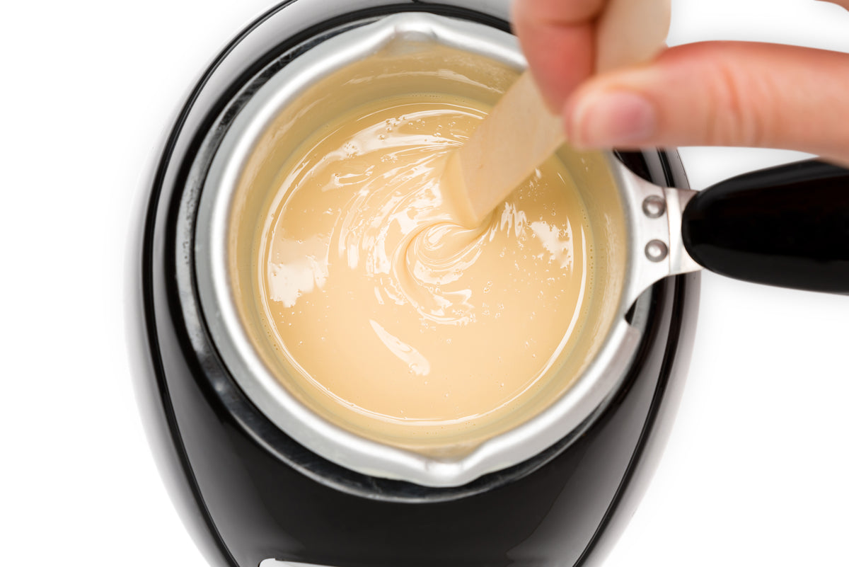 deluxe soft creme wax pot inside wax heater and mixed by a spatula