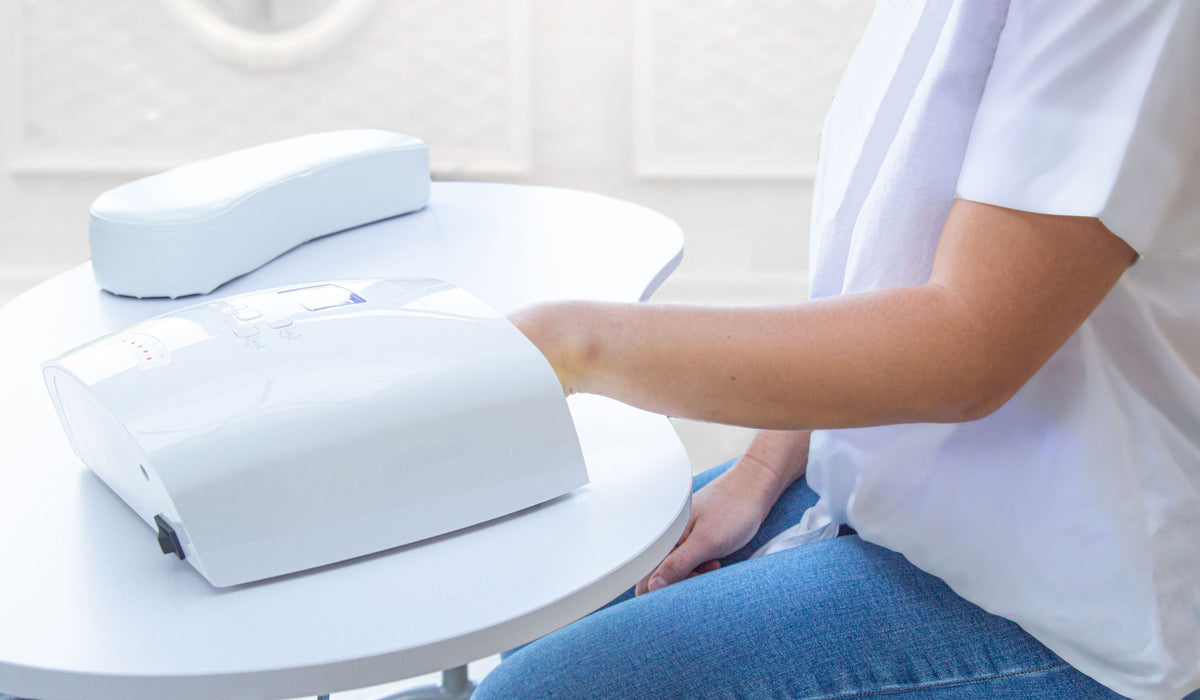 A person uses the Rio Professional Manicure & Nail Beauticians Table, placing their hand inside a white manicure device for drying or therapy. Another device case sits on the clean, modern table.