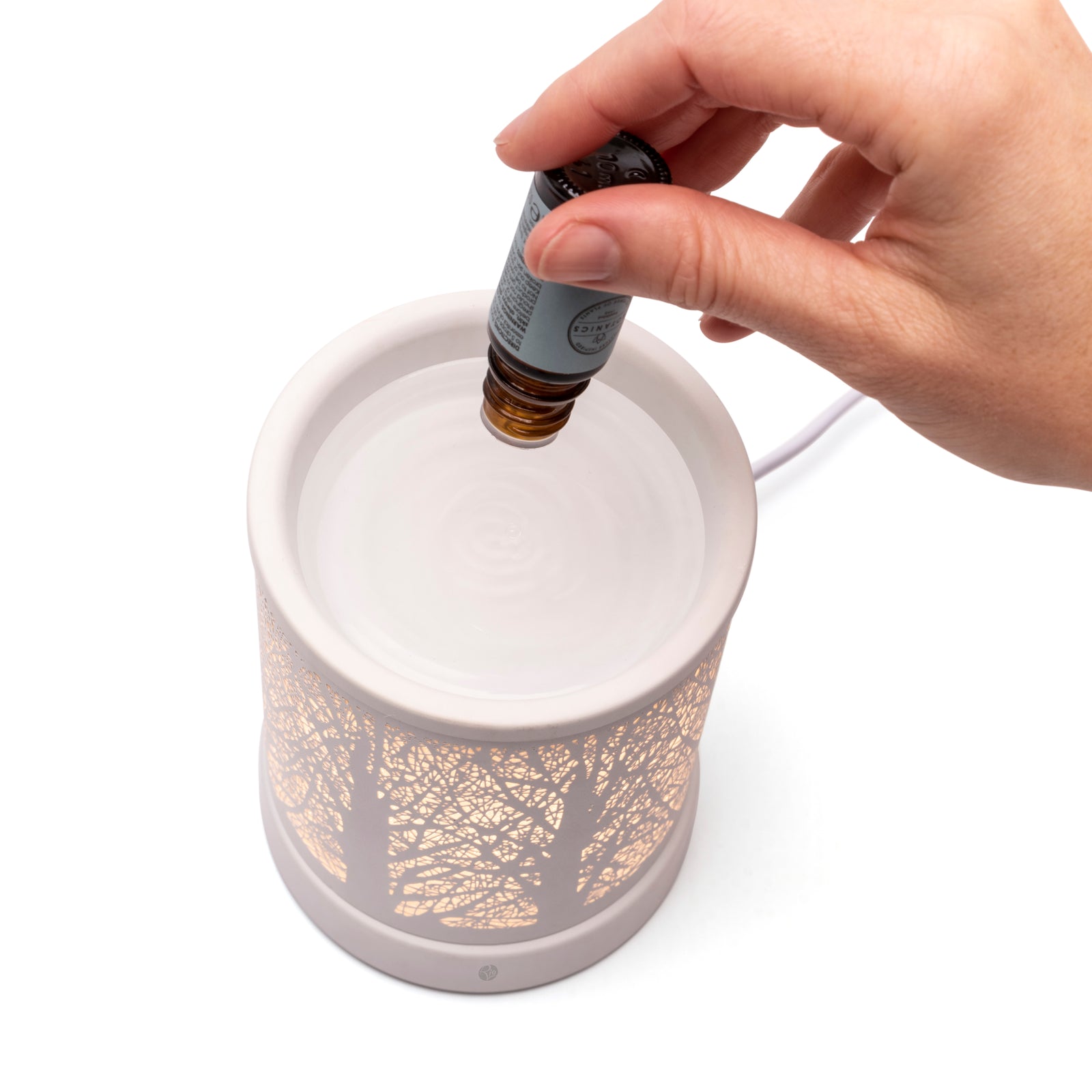 A hand pours liquid into the top of the Rio FORA Wax Melt Burner & Aroma Diffuser Lamp, whose decorative tree pattern and soft glow offer a stylish way to relax.
