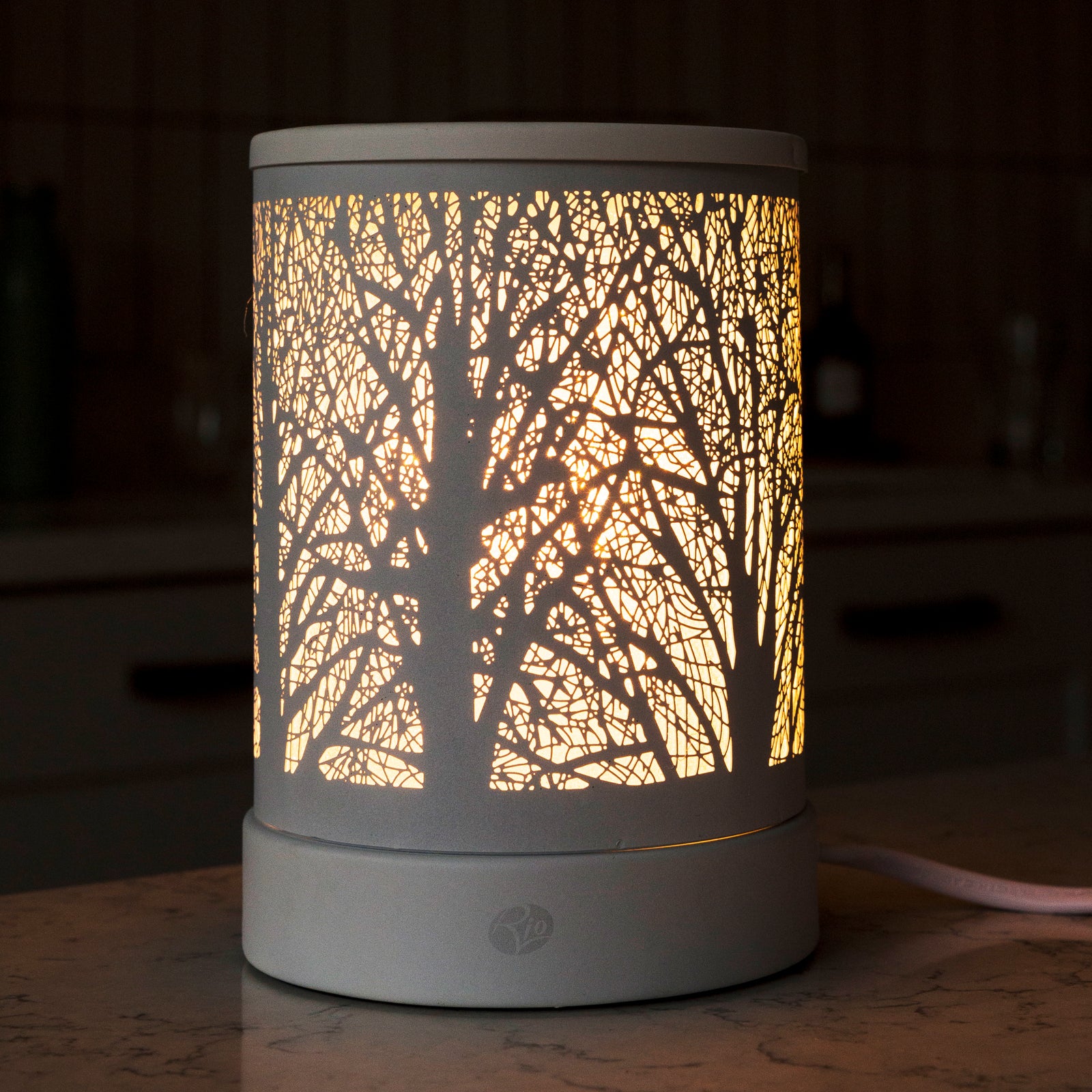 The Rio FORA Wax Melt Burner & Aroma Diffuser Lamp features a cylindrical shade with an intricate tree branch pattern, emitting a warm glow—ideal for creating a stylish, relaxing ambiance on any surface.