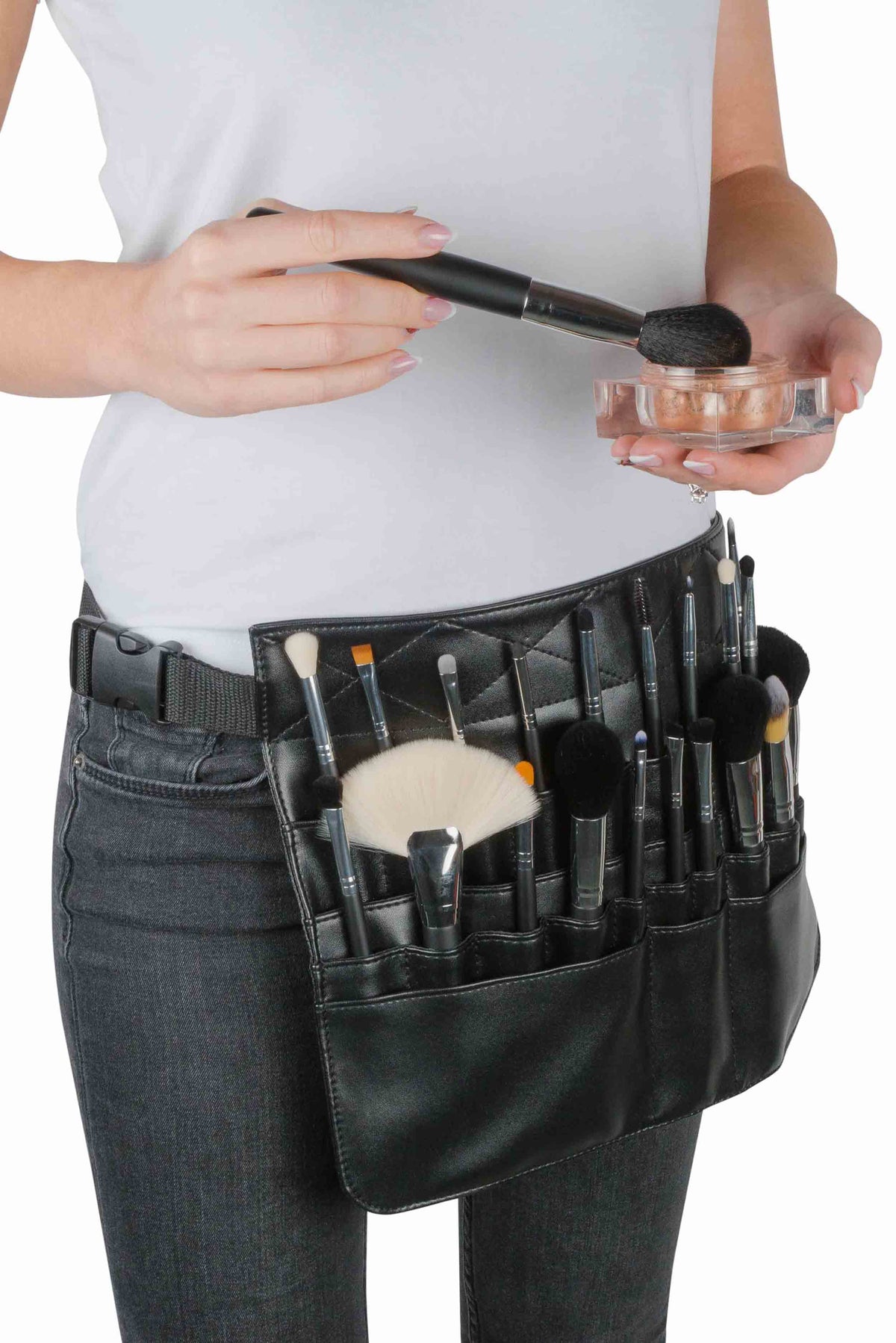 Wearing a Rio PROFESSIONAL SALON MAKEUP BRUSH COLLECTION & BELT, a person in a white shirt and dark pants holds a powder container and applies powder with one of the brushes.