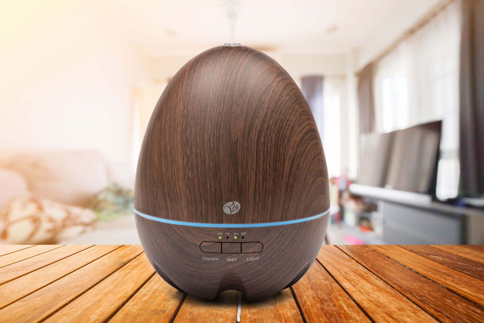 The Rio ARIA Aroma Diffuser Humidifier and Nightlight rests on a wooden table in a softly lit living room, enhancing relaxation and décor as sunlight pours through large windows in the background.